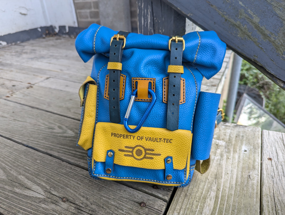 Handcrafted full grain leather mini roll top bag in blue and yellow vault colors with dual buckle straps and carabiner