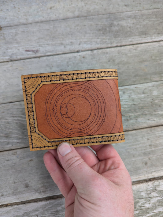 Hand holding a brown leather wallet with circular design on a wooden surface